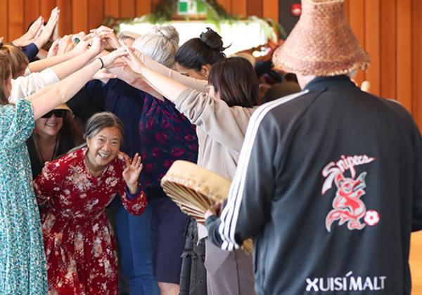 A group of people making a bridge with their hands joined. A woman passes below the bridge. 