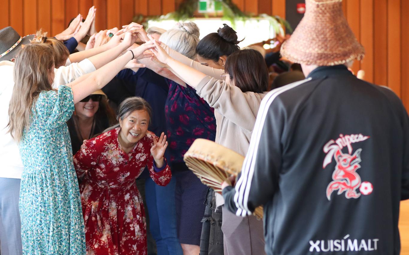 A group of people create a bridge by holding hands. A woman passes beneath the bridge. 